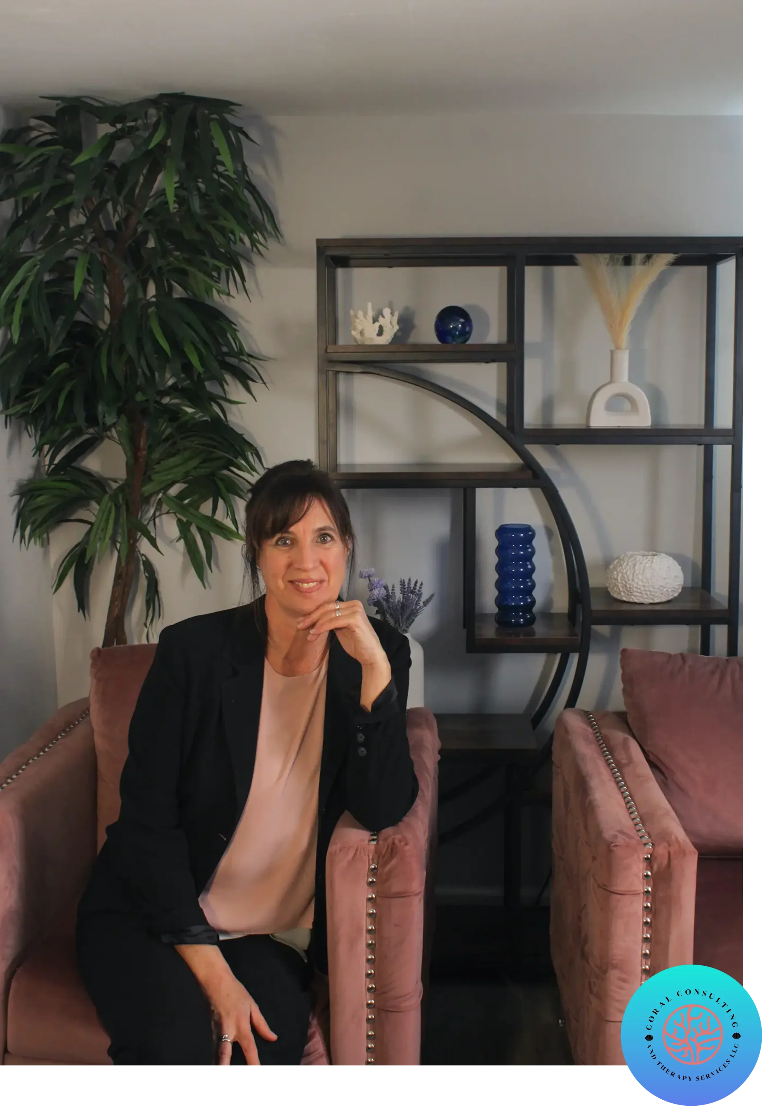 Woman sitting on a pink couch with a bookshelf behind her.