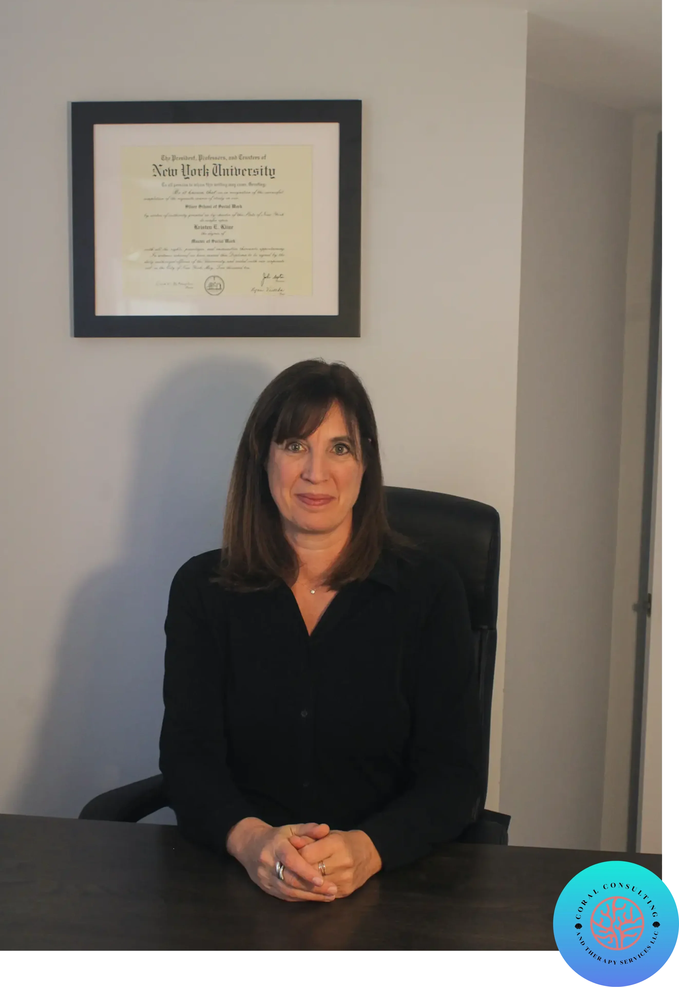 Professional woman sitting in an office chair with a framed diploma on the wall.