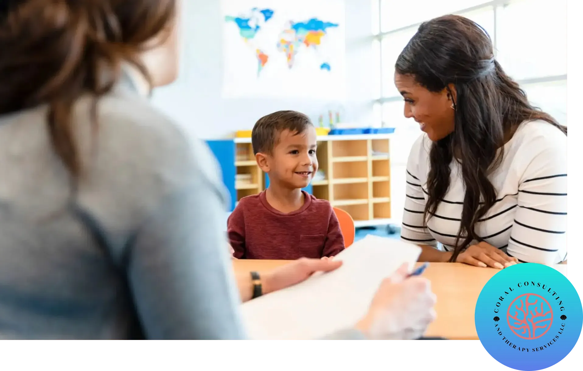 A young boy smiles while talking to two adults in a classroom.