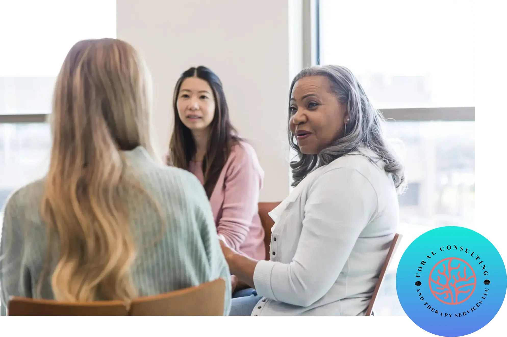 Three women engaged in a thoughtful conversation in a bright room.